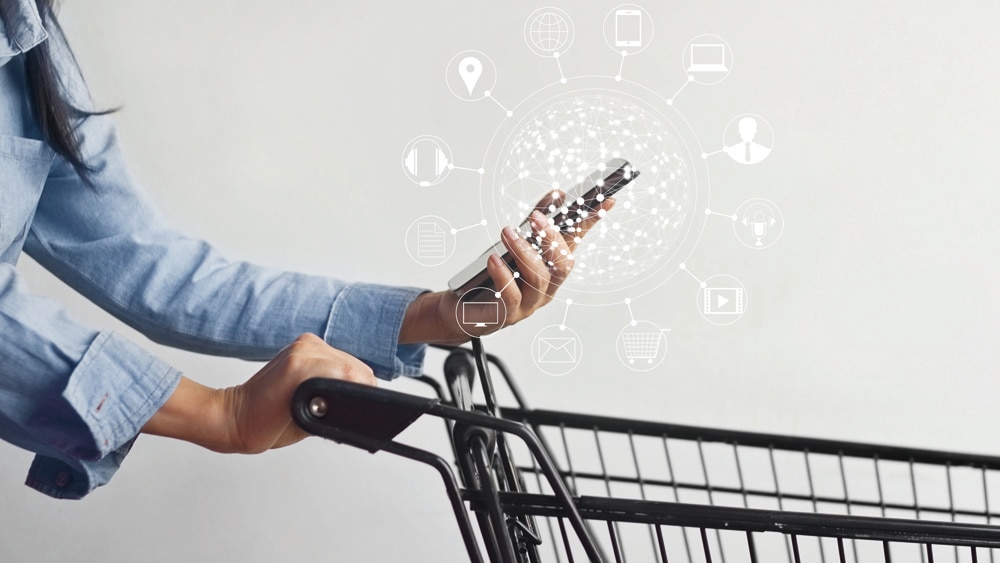 E-handelslogistik En person i skjorta står med en kundvagn och tittar på sin mobiltelefon